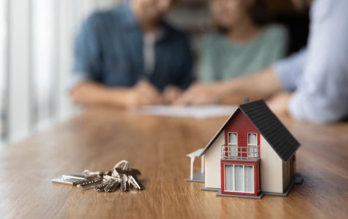 Small house with house keys. Owners signing home loan in the background.